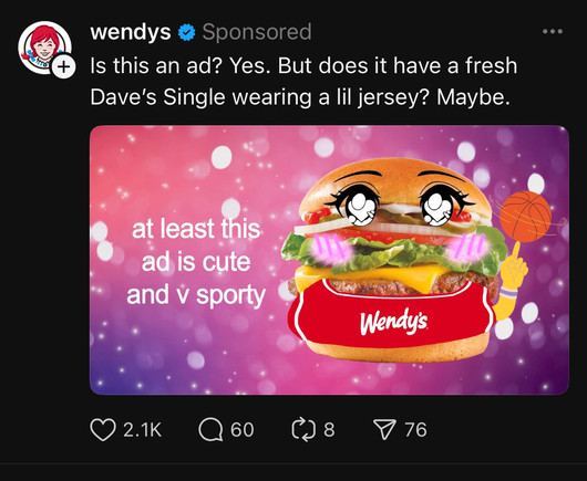A sponsored advertisement from Wendy’s on Threads. The ad features a stylized Dave’s Single burger, edited with exaggerated anime-style eyes, blushing cheeks, and a Wendy’s-branded sports jersey. The burger is also depicted with cartoonish arms, one of which is spinning a basketball. The background is pink with sparkles, giving it a playful aesthetic. The text on the image reads, “at least this ad is cute and v sporty.” Above the image, the caption from Wendy’s humorously acknowledges that it is indeed an ad, stating, “Is this an ad? Yes. But does it have a fresh Dave’s Single wearing a lil jersey? Maybe.” The post has engagement metrics at the bottom, including 2.1K likes, 60 comments, 8 reposts, and 76 saves, indicating user interaction.