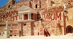 Scene from the movie The Life of Brian. There are ancient buildings in the background covered with multiple graphities saying 'Romani ite domum' meaning "Romans, go home!'