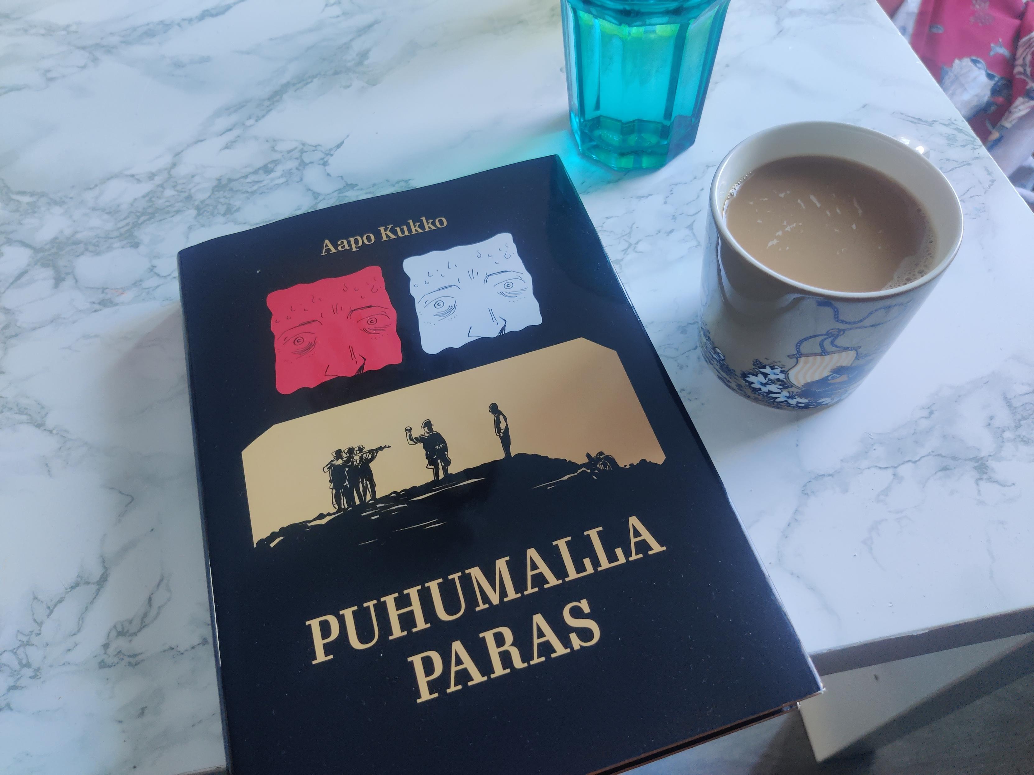 Aapo Kukon sarjakuva Puhumalla paras, sekä kahvikuppi.