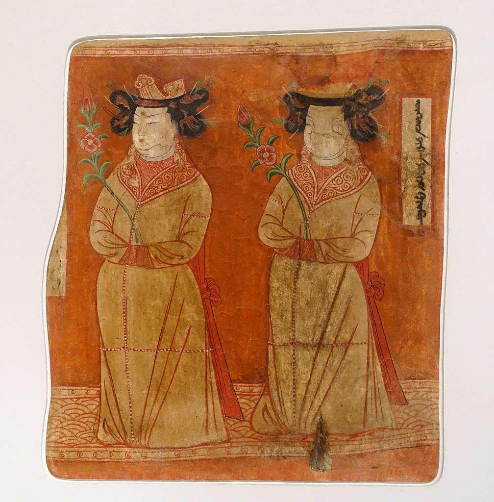 Valokuva keskiaikaisesta maalauksesta, joka esittää kahta ylellisesti puettua naista, joilla on monimutkaiset hiuslaitteet. Naisten musta tukka on letitetty ja kieputettu kahdeksikoksi kummallakin puolella päätä. Silmukoista pistää esiin käyriä hiusneuloja. Hiuksiin on kiinnitetty pilvien ja lintujen muotoisia koristeita. Naisilla on kultainen päähine tai kruunu päälaella. Kruunuista roikkuu pitkiä punaisia nauhoja naisten selkää pitkin. Nauhat on solmittu yhteen lanteiden kohdalla ja ne ulottuvat melkein maahan asti. Molemmilla naisilla on lähes valkoinen iho, kapeat mustat silmät ja ohuet mustat kulmakarvat, kapea suora nenä ja pienet pyöreät huulet. Heillä on pitkät roikkuvat korvakorut ja koristeelliset kaulukset. Heidät on puettu samanlaisiin kullanruskeisiin asuihin, joissa on maahan asti ulottuva helma ja helmikirjailua muun muassa hihoissa. Molemmat naiset ovat työntäneet kätensä toisen käden hihaan ja pitelevät samalla vatsaansa vasten pitkävartista punaista kukkaa, jossa on vihreitä lehtiä. Maalauksen taustaväri on oranssinpunainen. Naiset seisovat koristeellisen nauhan päällä, jossa on pyöreitä aaltokuvioita. Naisten vieressä on laatikko, johon on kirjoitettu muinaisuiguurilaisella kirjoituksella jotakin.