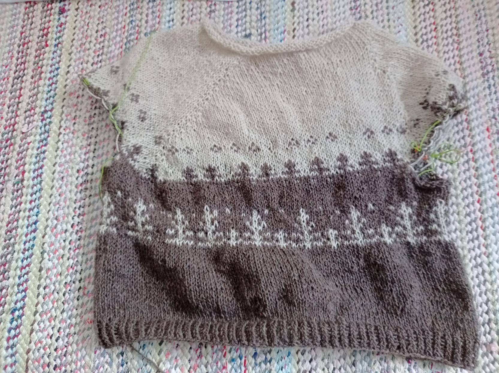 Keskeneräinen valko-ruskea villapaita, josta puuttuu vielä hihat ja jonka silmukoiden lisäykset menee ihan kierollaan.