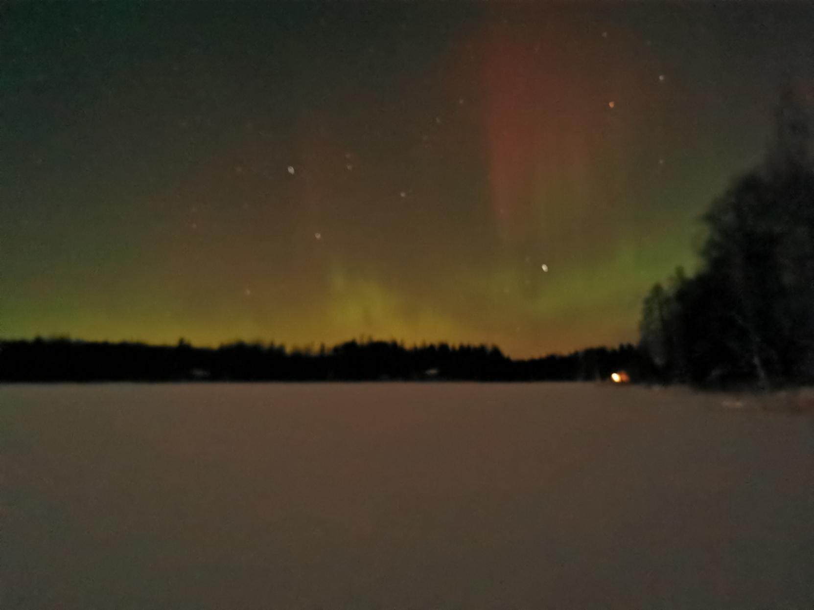 Dark lake with snow cover and above forest line Aurora Borealis.
