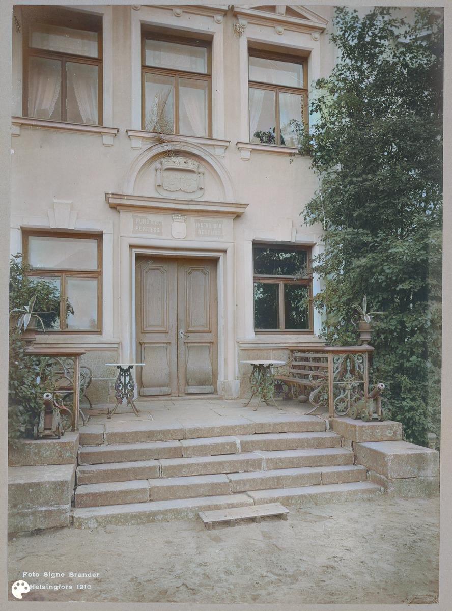 Suur-Sarvilahden kartanon sisäänkäynti Pernajassa. (1910, Museovirasto, Historian kuvakokoelma)

Alkuperäisen valokuvan on ottanut Signe Brander. Tämä kuva on keinotekoisesti väritetty DeOldify-algoritmilla.