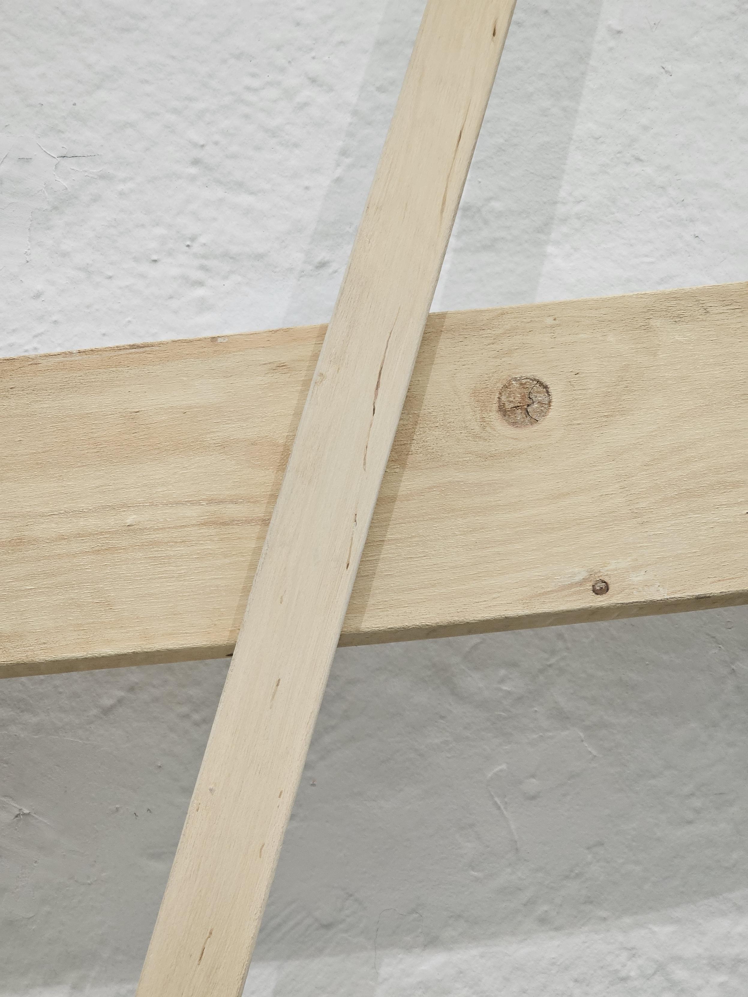 Kaksi laudan/puuriman näköistä asiaa ristissä. Yksityiskohta Antti Oikarisen taideteoksesta