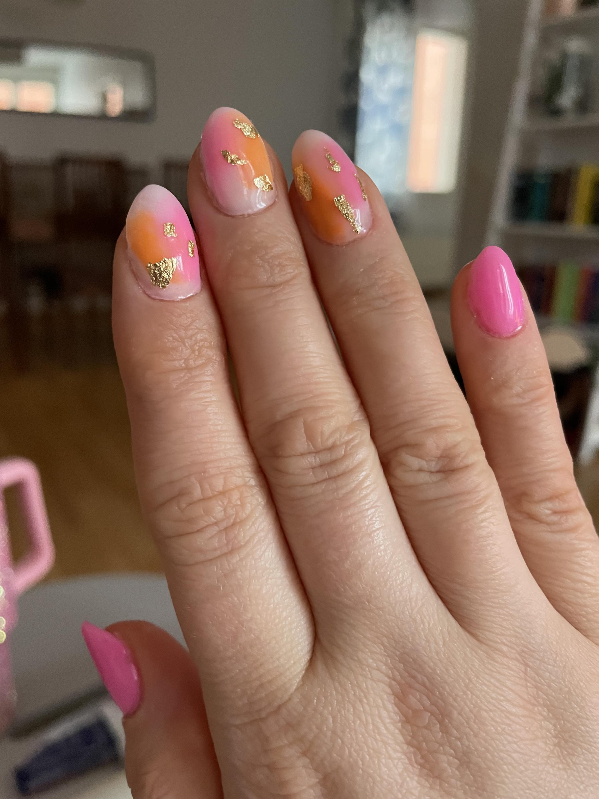 Oikea käsi sormet suoristettuna jossa peukalon ja pikkusormen kynnet vaaleanpunaiset. Keskimmäisten sormien kynnet ovat pohjaväriltään valkoiset ja niissä on oranssin ja vaaleanpunaisen värisiä siveltimen vetoja. Pieniä kultahippuja on liimattu kynnen pintaan, kolme kappaletta per kynsi. Kynsien pinta on kiiltävä ja tasainen.