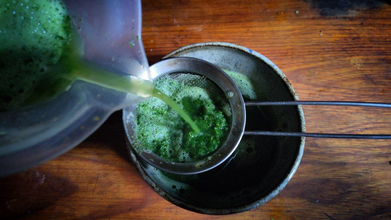 Un bol amb un colador a sobre on s'està abocant un batut verd