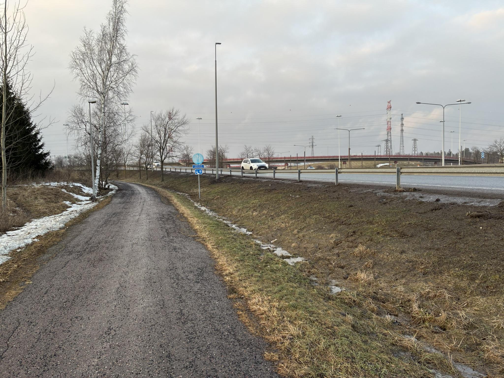 Mutainen pyörätie, ja oikealla moottorietieramppi ja muut osat eritasoliittymää. Kauempana ovat sähköpylväät johtoineen.