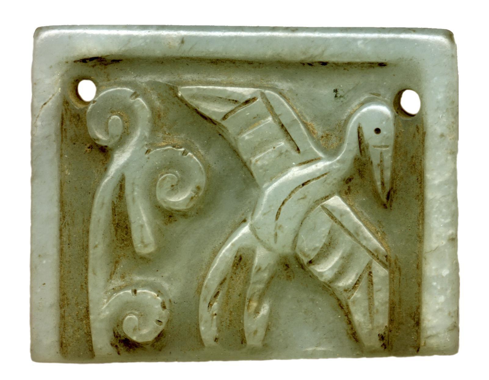 Valokuva esittää vihreää suorakulman muotoista kivilaattaa, johon on kaiverrettu spiraalin muotoisia kuvioita sekä lentävän kurjen kuva. Kivilaatan yläkulmiin on porattu reiät, jotta sen voi kiinnittää johonkin (ehkä vyöhön).