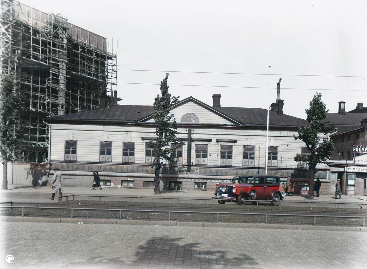 Heikinkatu 15 (=Mannerheimintie 9). (1937, Helsingin kaupunginmuseo)

Alkuperäisen valokuvan on ottanut Signe Brander. Tämä kuva on keinotekoisesti väritetty DeOldify-algoritmilla.