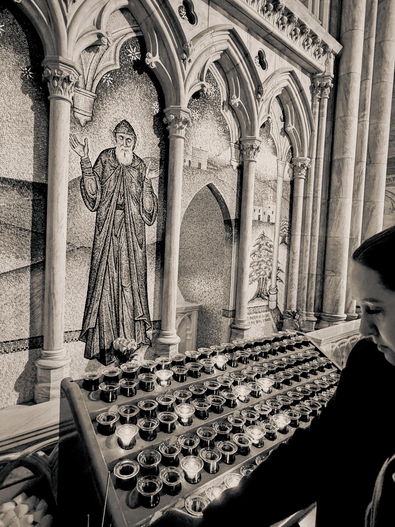 inside a cathedral in NYC where a shadowed woman lights a votive at a tilede depiction of st patrick — black and white
