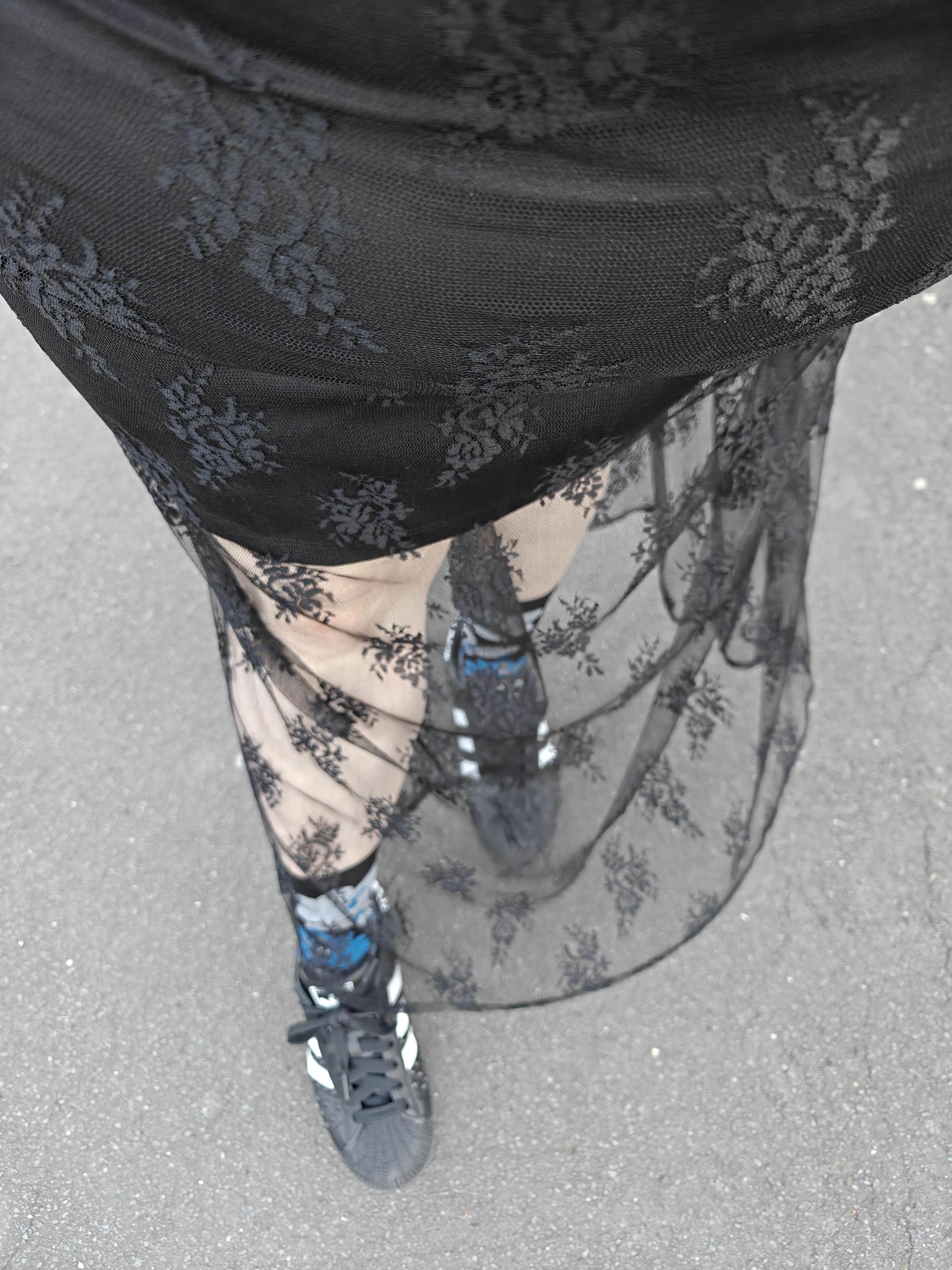 Looking down at my outfit. A short black slip mini skirt covered by black mesh lace with a floral pattern. My crew socks are blue, grey and black floral patterned and I'm wearing spiky black and white Adidas Superstar trainers.