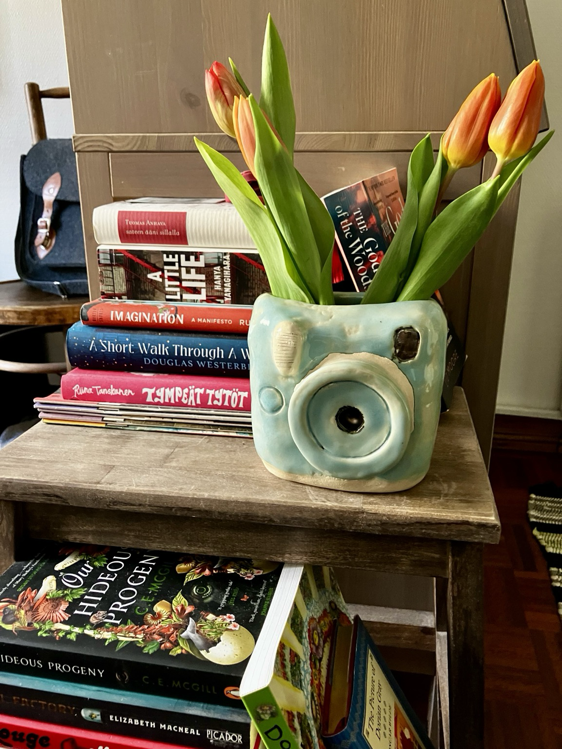 Tulppaaneja vaaleansinisen polaroid-kameran näköisessä maljakossa, kirjapinon edessä.