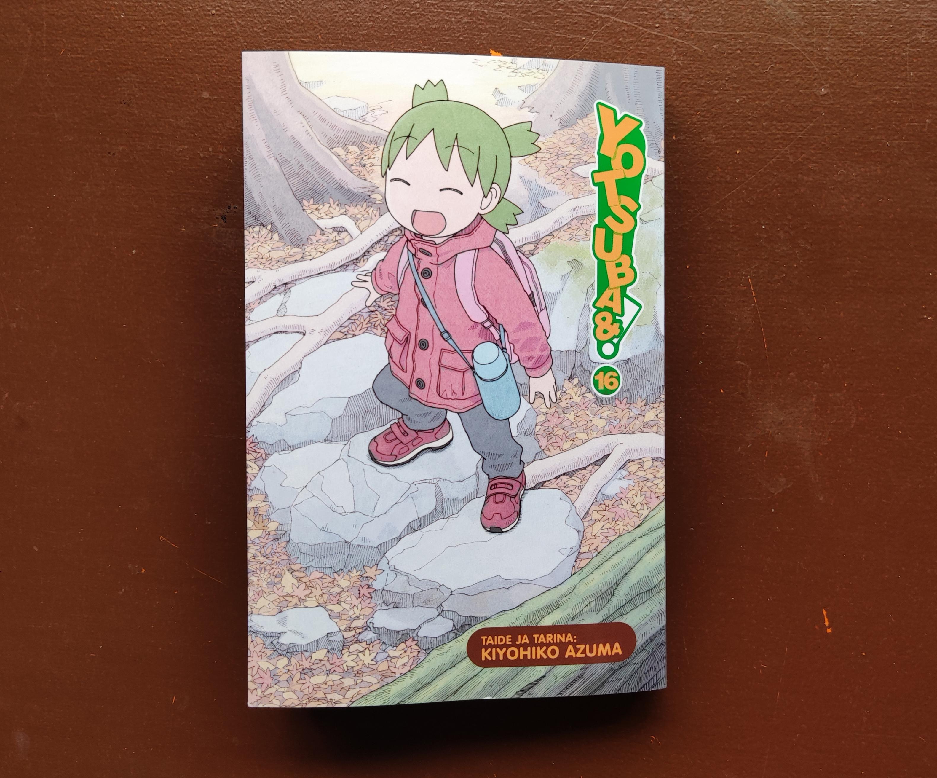 Yotsuba&! sarjan 16. pokkari ruskealla taustalla. Kannessa vihreätukkainen Yotsuba hymyilee silmät kiinni ja suu auki ja seisoo kahdella kivellä.