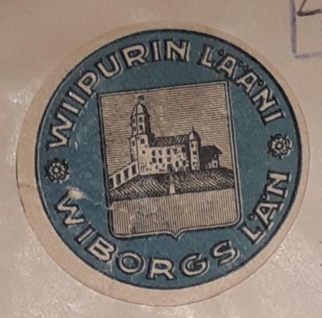 Viipurin läänin vaakuna 1920-luvun alusta ja sitä ympäröivä teksti: Wiipurin lääni - Wiborgs län. Väri: Musta ja sininen. Vaakunassa on Viipurin linna.