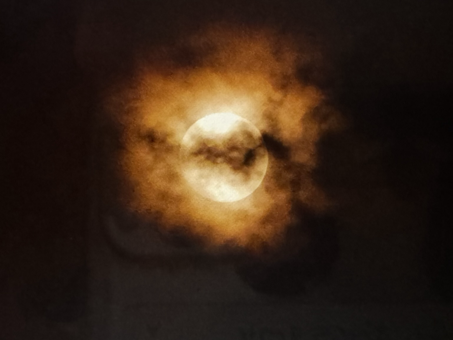 Full moon surrounded by clouds. The moon has a reddish aura that illuminates the shadows of the clouds in a way that mesmerizes