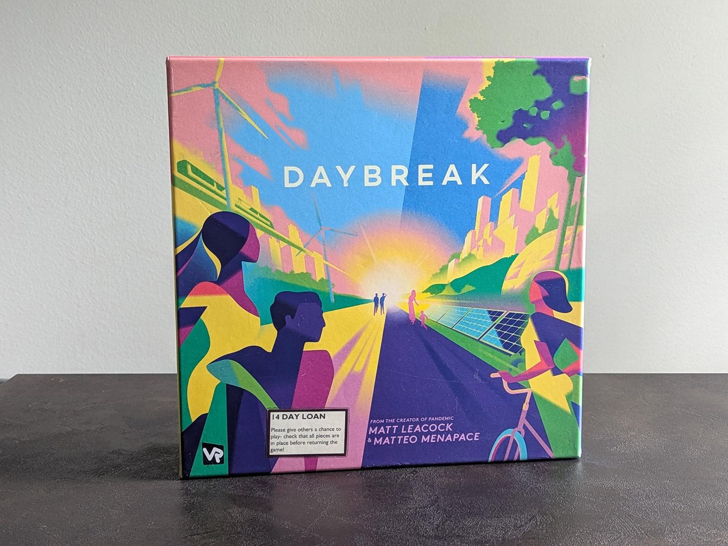 Daybreak-lautapelin laatikko. Laatikon kansi on kuvitettu vektorigrafiikalla. Kuvassa näkyy kauas horisonttiin katoava jalkakäytävä, jonka laidalla on tuulimyllyjä, aurinkopaneeleita sekä yläilmoissa kulkeva juna.