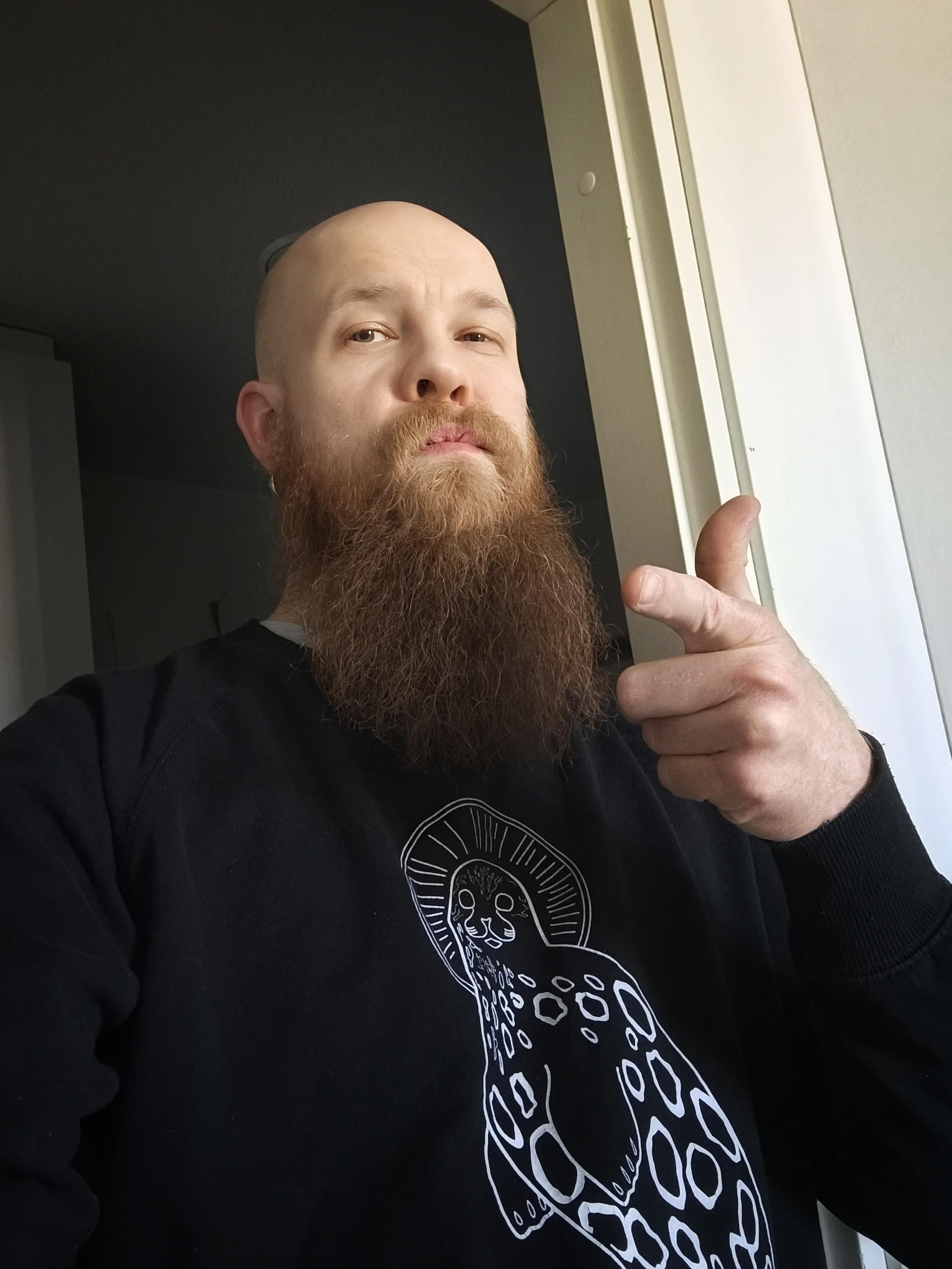 Parrakkaan miehen selfie. Oikean käden etusormella osoitan kohti kameraa. Päällä musta "Save the norps" -paita.