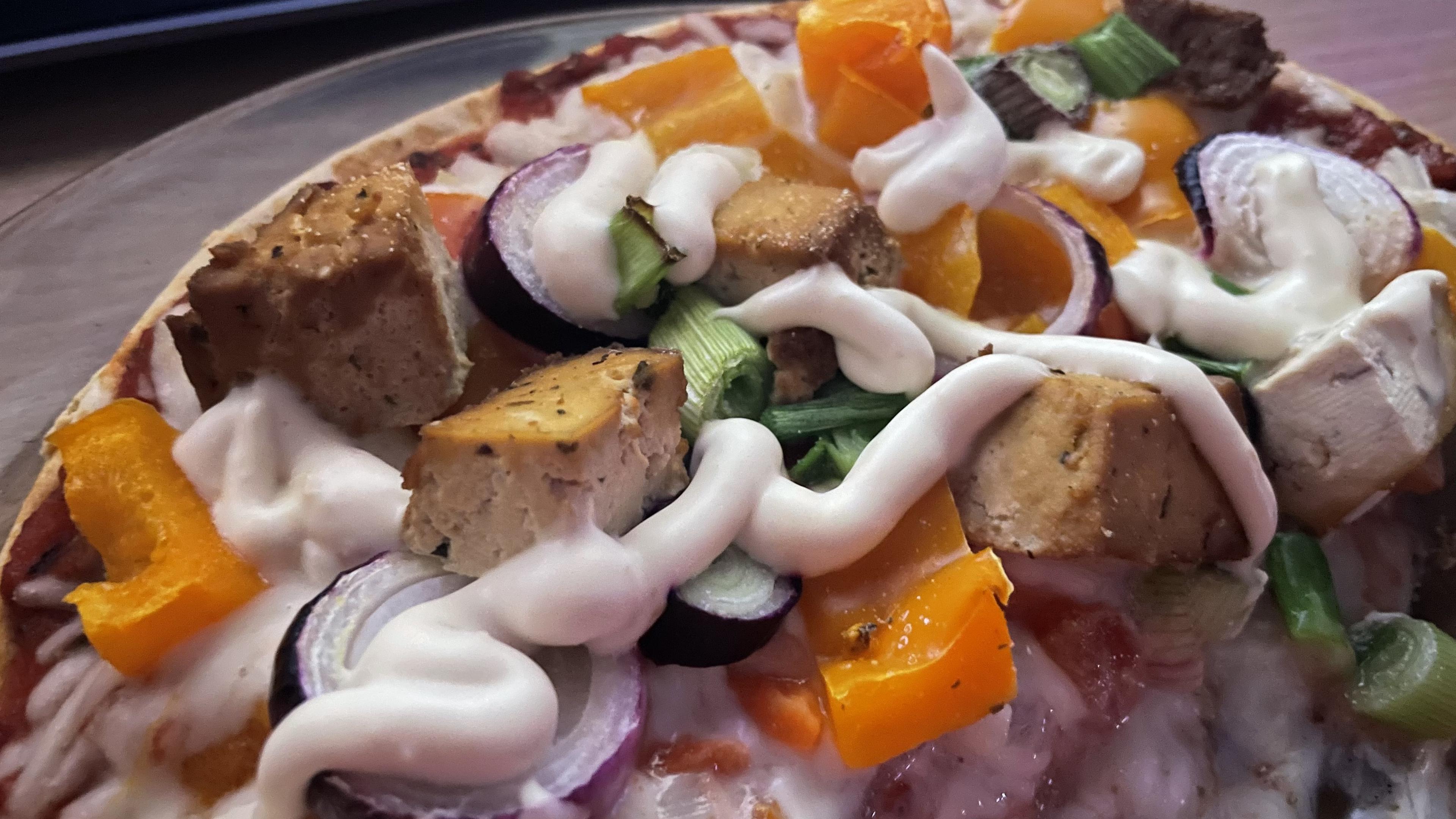 Lähikuva valmistamastani pizzasta, jossa näkyy kauniin kullanruskeaksi paistunutta tofua, oranssia paprikaa, sipulin varsiosasta leikattuja viipaleita ja vegaanista majoneesia.