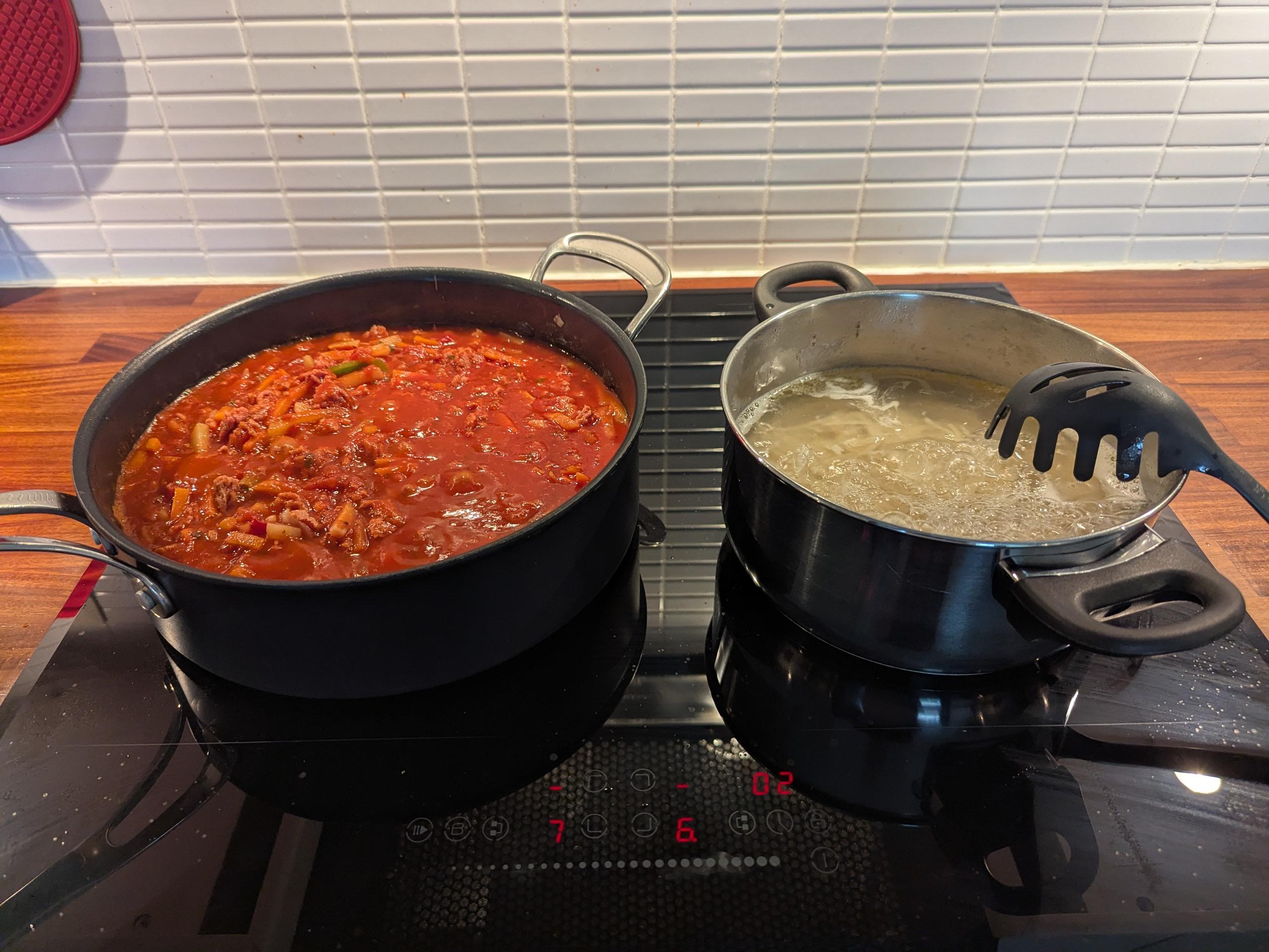 Liedellä poriseva kasari, joka on täynnä tomaattipohjaista kastiketta. Sen vieressä toisessa kattilassa kiehuu spagetit.