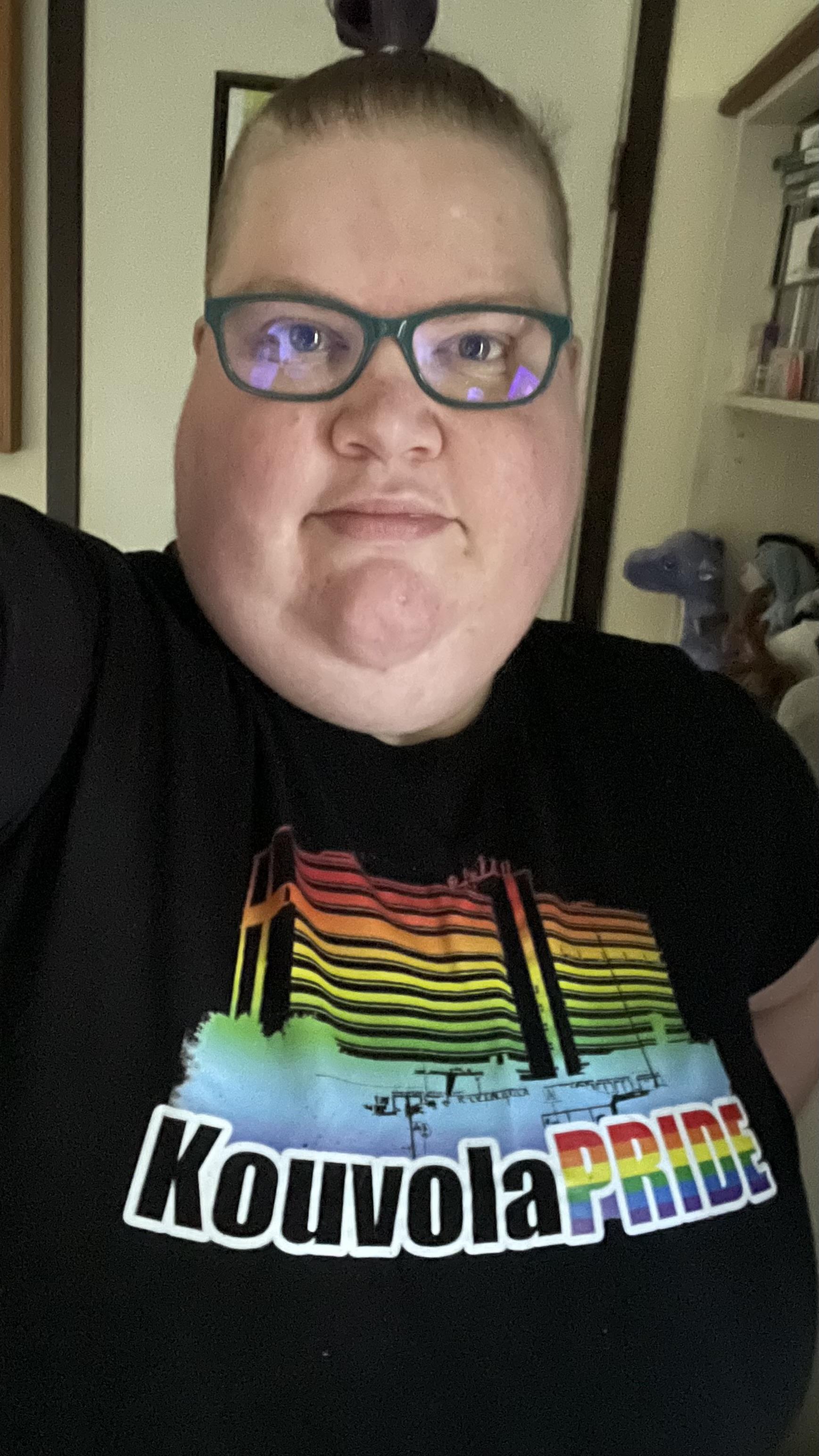 Selfie minusta, päälläni on musta Kouvola Pride -paita, jossa on sateenkaaren väreissä yksi kaupungin keskustan maamerkeistä, Kouvola-talo.