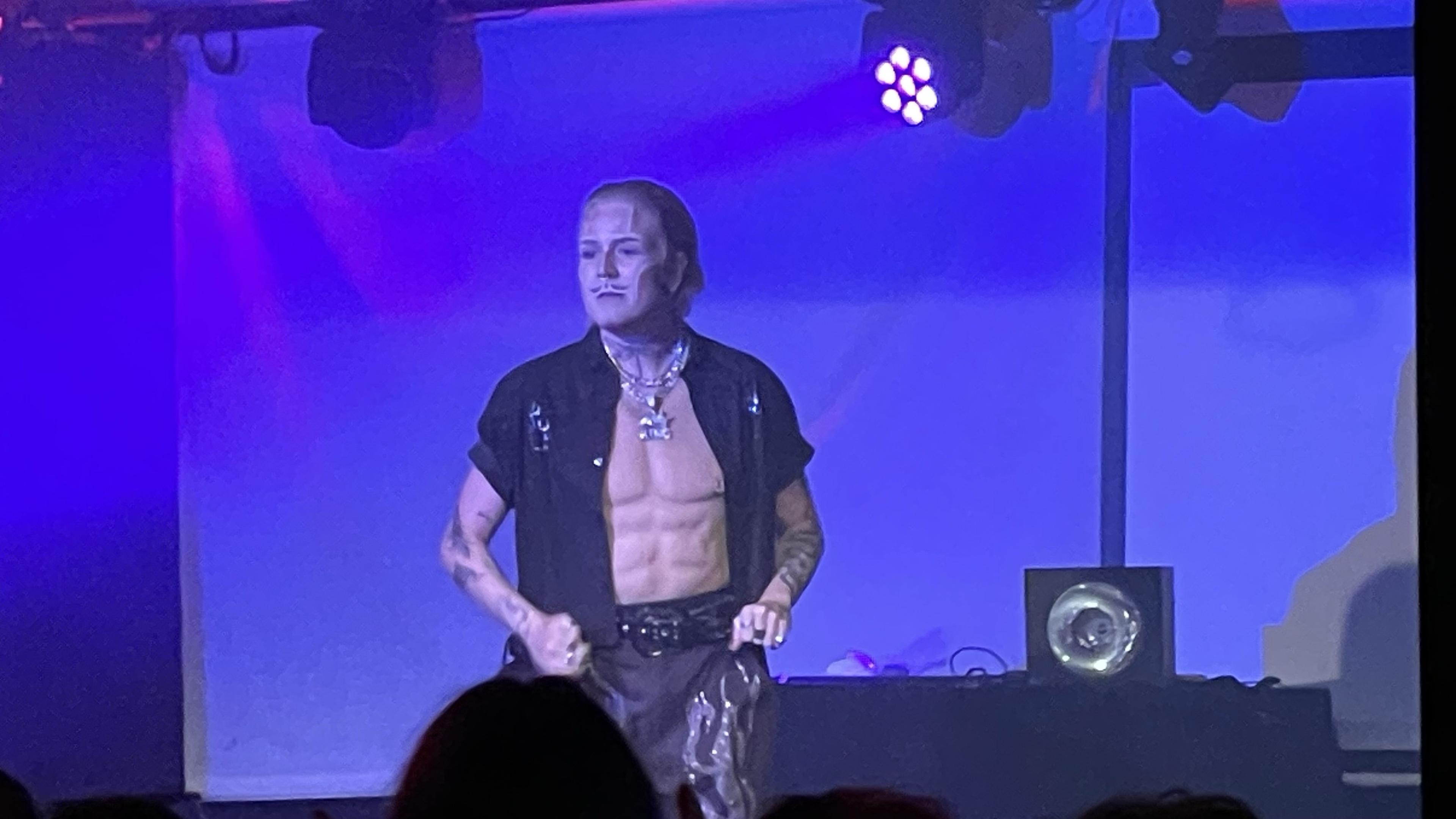 Whipher Snipher, drag king lavalla. Mustaan paitaan ja housuihin sonnustautunut henkilö, naisoletettu pukeutuneena mieheksi.