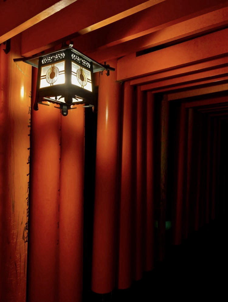 A lantern hanging from a tunnel of red torii gates in Fushimi Inari Taisha, Kyoto at night